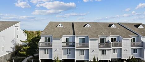 A multi-story residential building with balconies, a parking lot, and a clear sky.