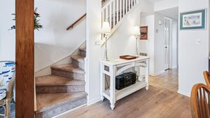 Een trap met een witte leuning, een witte console tafel met speakers, en een houten vloer.