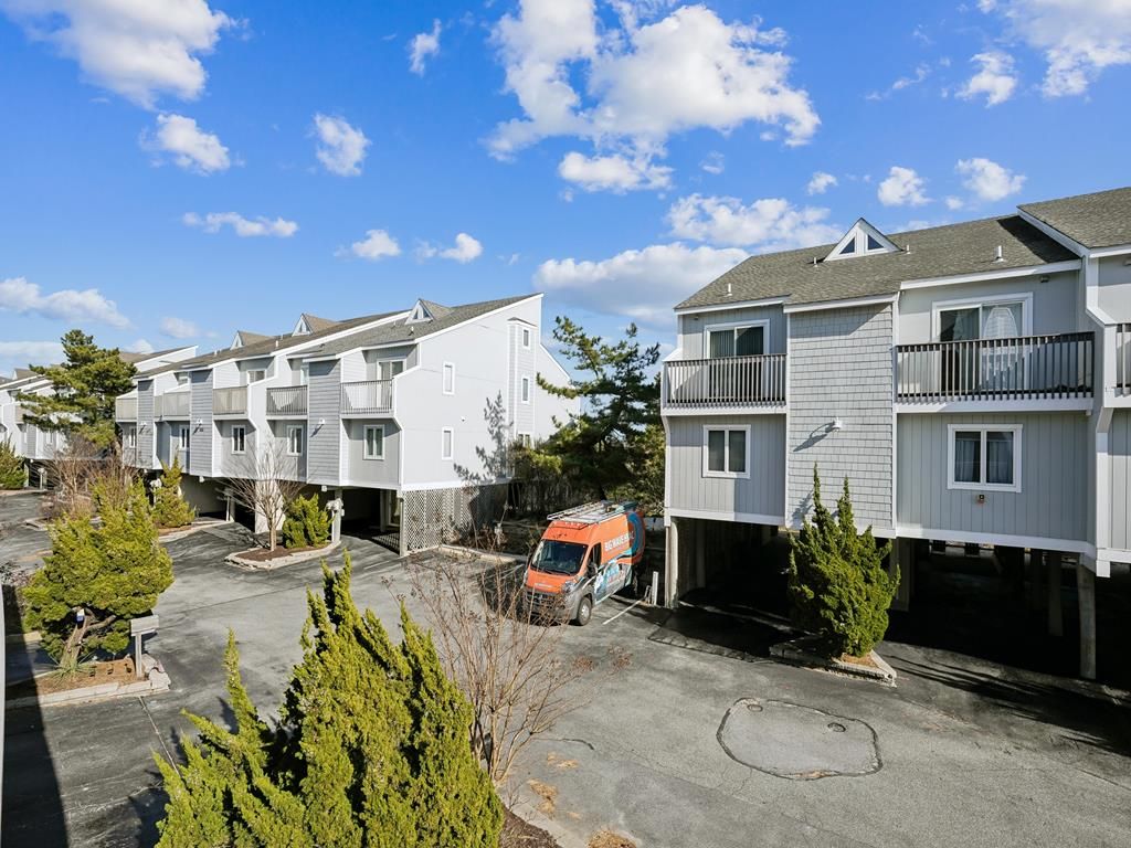 A row of residential buildings with balconies, a parking area, and a van parked in front.