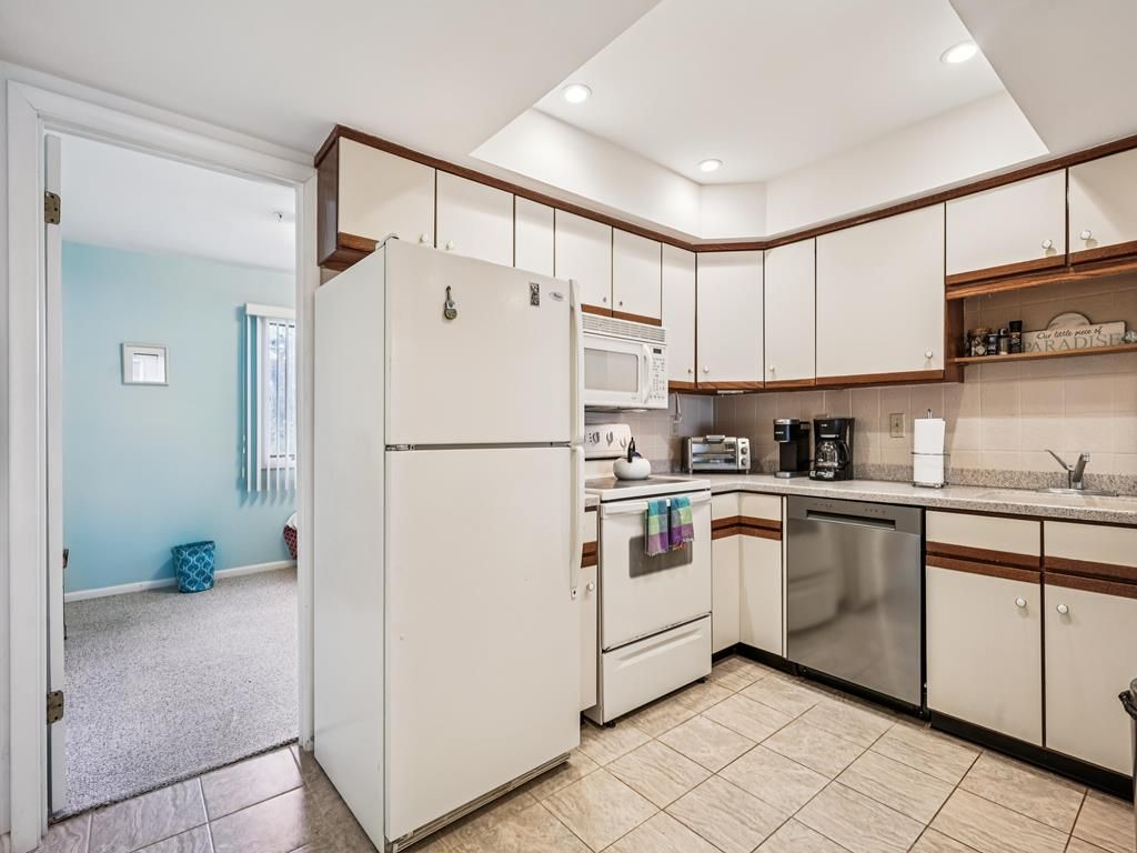 Una cocina con armarios blancos, un refrigerador, un microondas, un tostador y un lavavajillas.