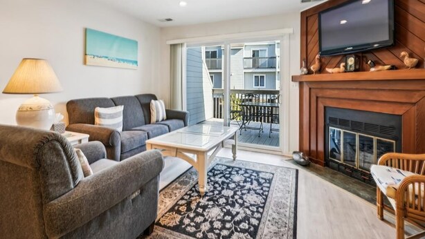 Een woonkamer met een bank, een salontafel, een televisie, een open haard en een balkon met tuinmeubels.