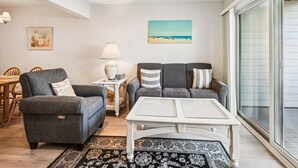 Een woonkamer met een bank, fauteuil, salontafel en een schilderij aan de muur.