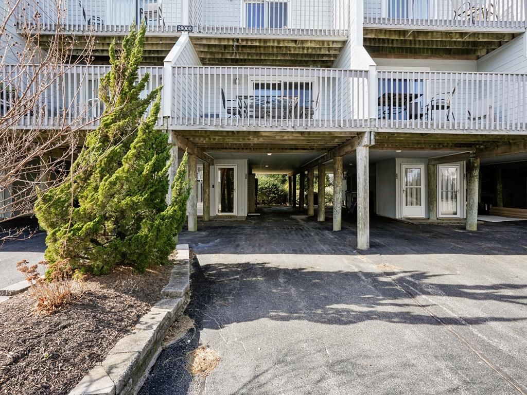Un edificio a più piani con un'area di accesso coperta, un piccolo albero e un vialetto lastricato.