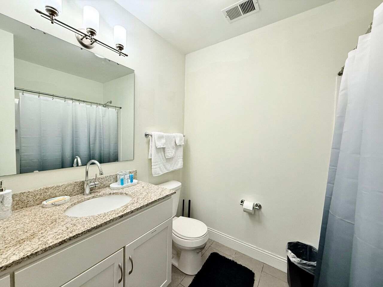 A bathroom with a double sink, a toilet, a mirror, and a shower curtain.