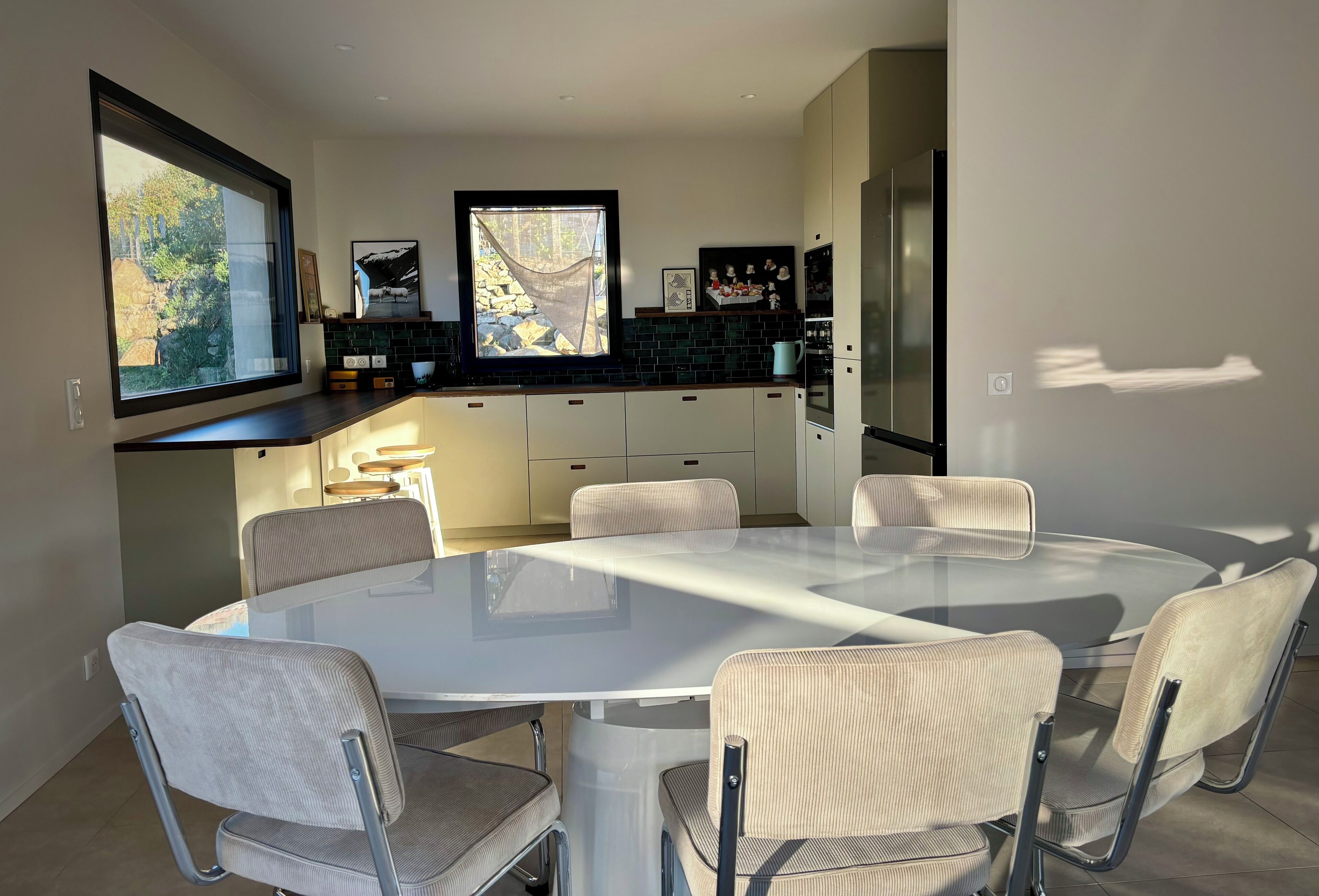 Una cocina moderna con una isla grande, armarios blancos y una zona de comedor con mesa de vidrio y sillas acolchadas.