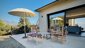 Ein Außenbereich zum Sitzen mit Holzkästen und einem Tisch, einem großen Sonnenschirm und Blick auf Berge.