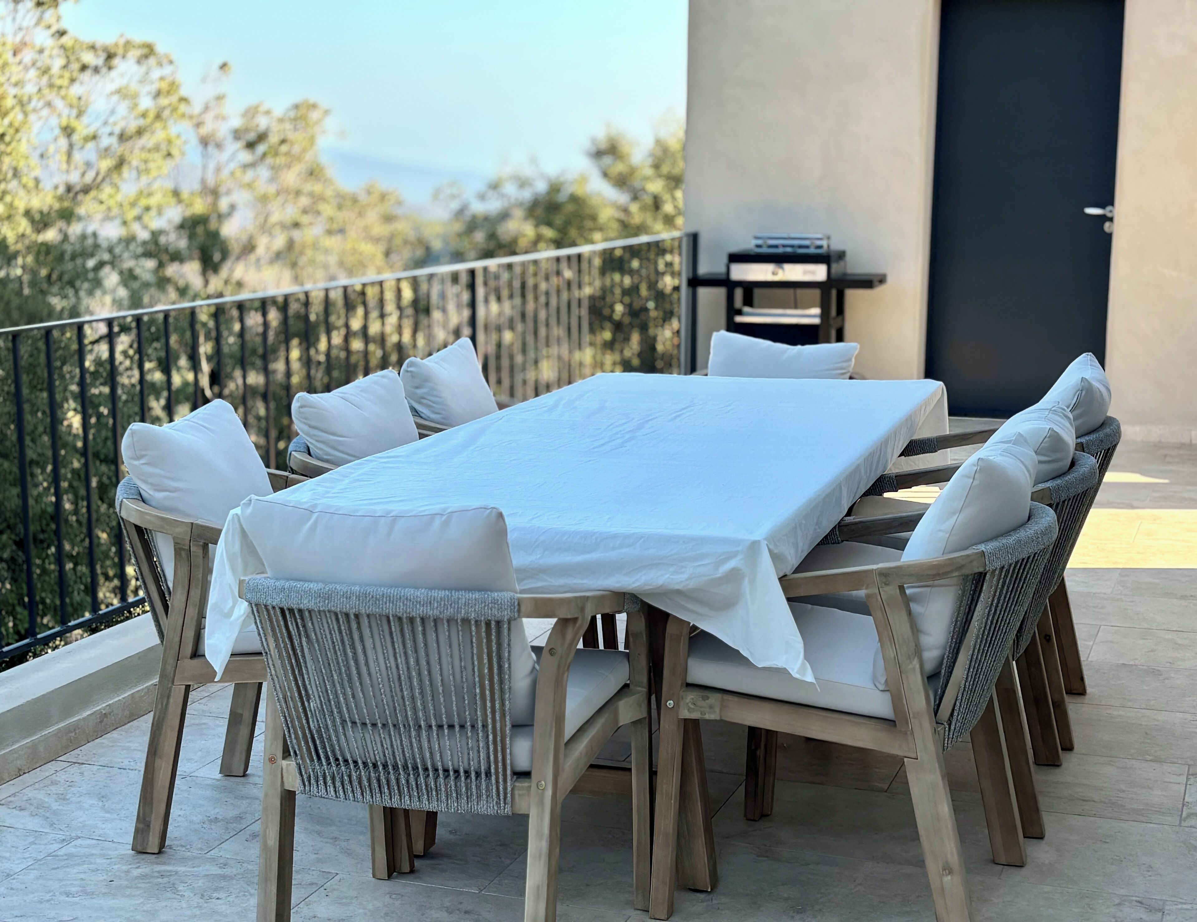 A dining area with a table set for four, surrounded by wicker chairs with cushions.