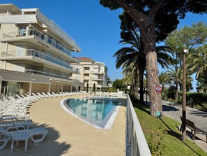 A poolside area with lounge chairs, a swimming pool, and a multi-story building with balconies. - Terrace & Pool Just Steps from the Beach (Cannes)