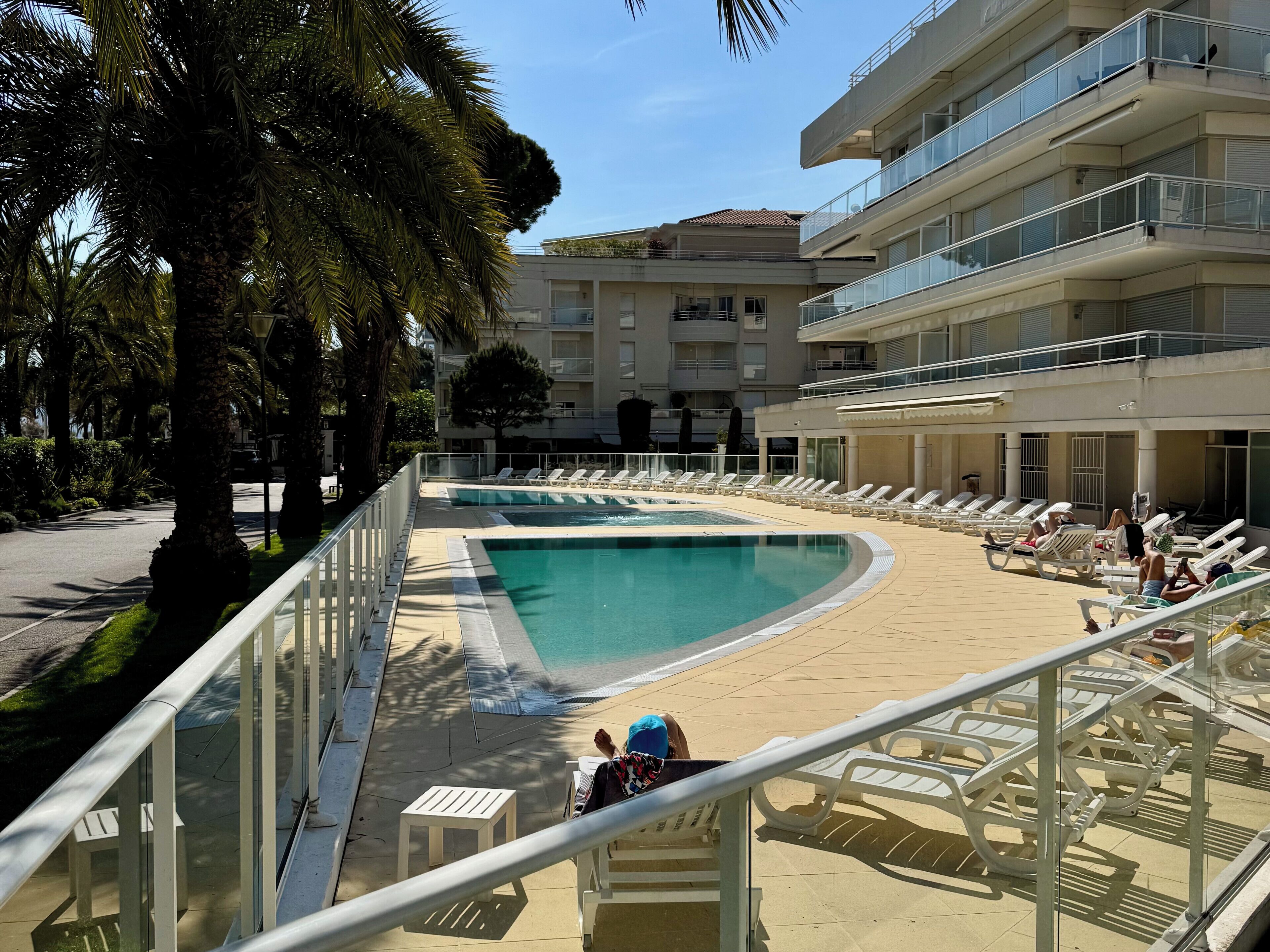 A pool area with lounge chairs, a small pool, and a building with balconies.