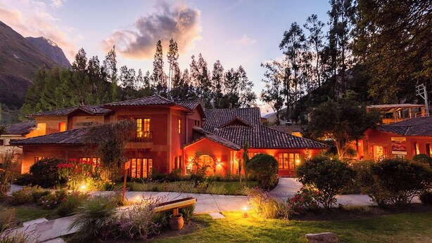 Une grande maison à plusieurs étages, avec un toit recouvert de tuiles rouges, entourée d’une végétation luxuriante et d’arbres.