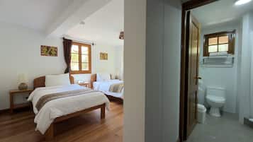 Une chambre avec deux lits, une fenêtre avec des rideaux, une table de chevet avec une lampe, et une salle de bain avec des toilettes et un lavabo.