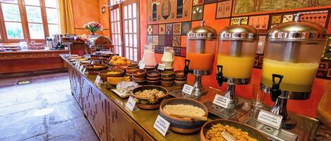 Un bufé con diversos alimentos y bebidas, incluyendo cereales, granola y dispensadores de jugo.