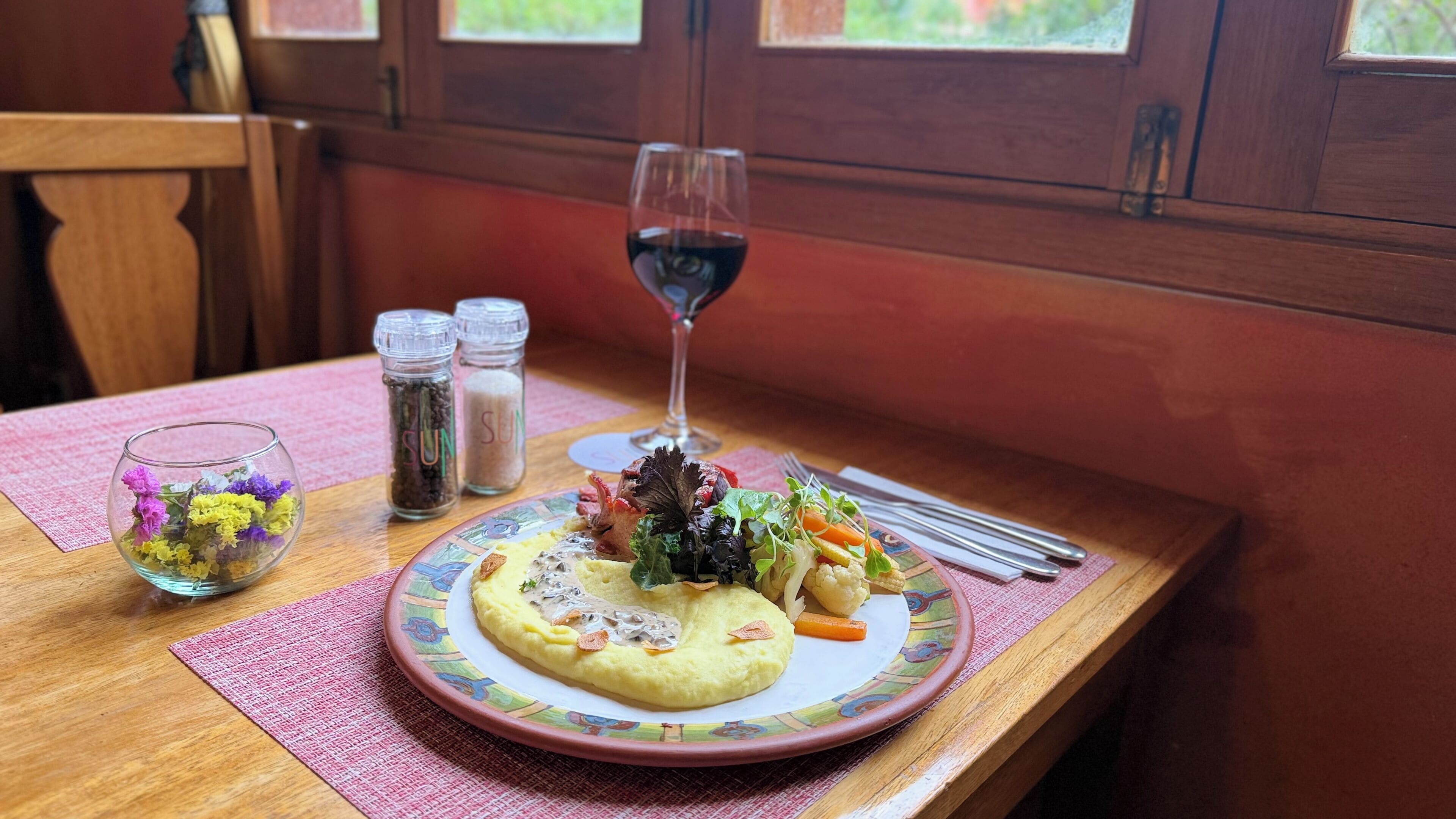 Una mesa con un plato de comida, una copa de vino tinto y dos saleros.