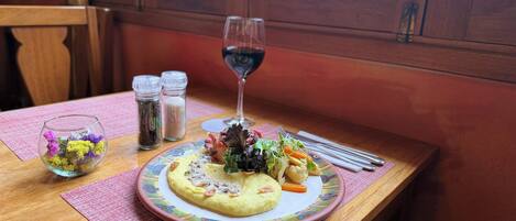 Una mesa con un plato de comida, una copa de vino tinto y dos saleros.