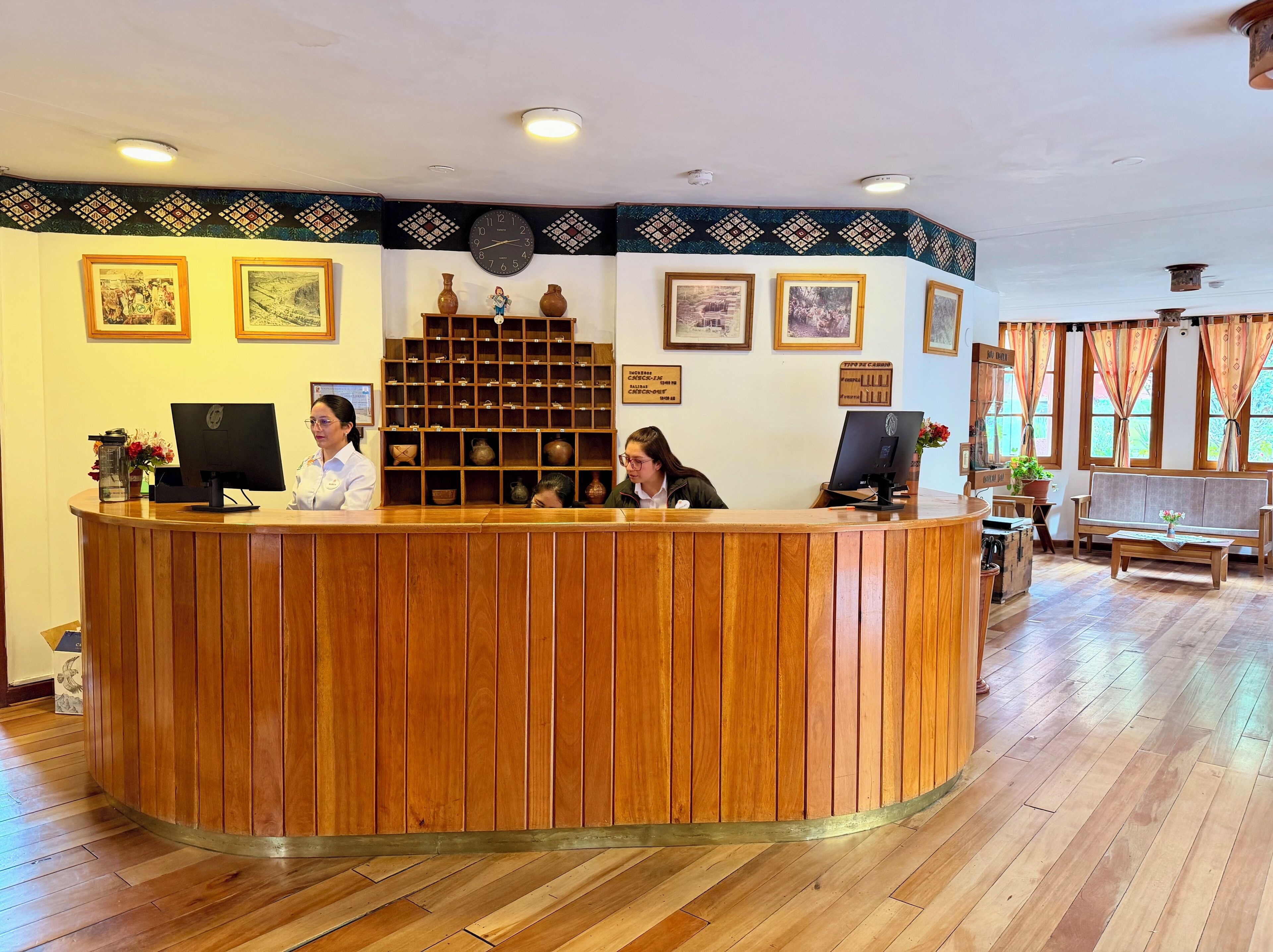 A reception desk with two monitors, a clock, and framed pictures on the wall.