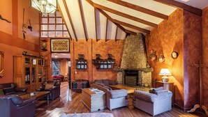 Un salon chaleureux avec un plancher en bois, des meubles en cuir, une cheminée en pierre et un plafond haut avec des poutres apparentes.