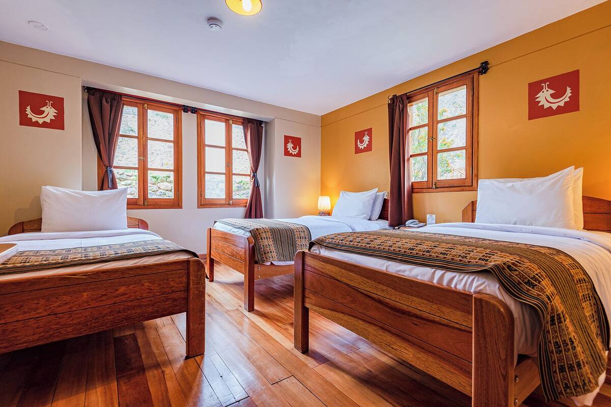 Una habitación de hotel con tres camas de madera, un escritorio de madera y una ventana con cortinas.