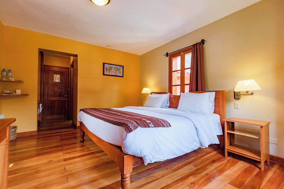 Un dormitorio con una cama de madera, un mesita de noche de madera, una puerta y una lámpara fijada a la pared.