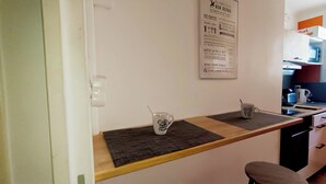 Een kleine kitchenette met een houten aanrecht, twee koffiemokken en een menukaart die aan de muur hangt.