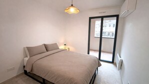 Un dormitorio con cama, mesita de noche, lámpara, luz de techo y puerta corrediza de cristal a un balcón.