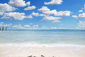 A beach with clear water, a sandy shore, and a blue sky with clouds. - Castaway on the Canal + Cabana Beach Club Included (Key Colony Beach)
