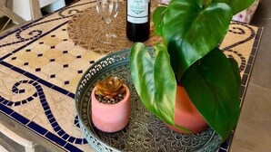 Quarto com uma cama, mesa de cabeceira, luminária, garrafa de vinho, copo e planta em vaso.
