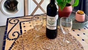 Uma cozinha com micro-ondas, chaleira e pia. Há uma garrafa de vinho e duas taças sobre uma mesa com toalha de mesa estampada.