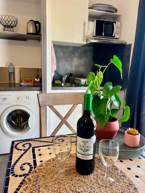 Une cuisine équipée d’un four à micro-ondes, d’une bouilloire et d’un évier. Une bouteille de vin et deux verres sont posés sur une table recouverte d’une nappe à motifs.
