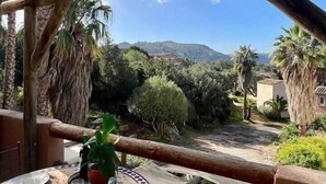 Uma área de refeições ao ar livre coberta, com uma mesa posta para dois, com vista para uma paisagem cênica com colinas e palmeiras.