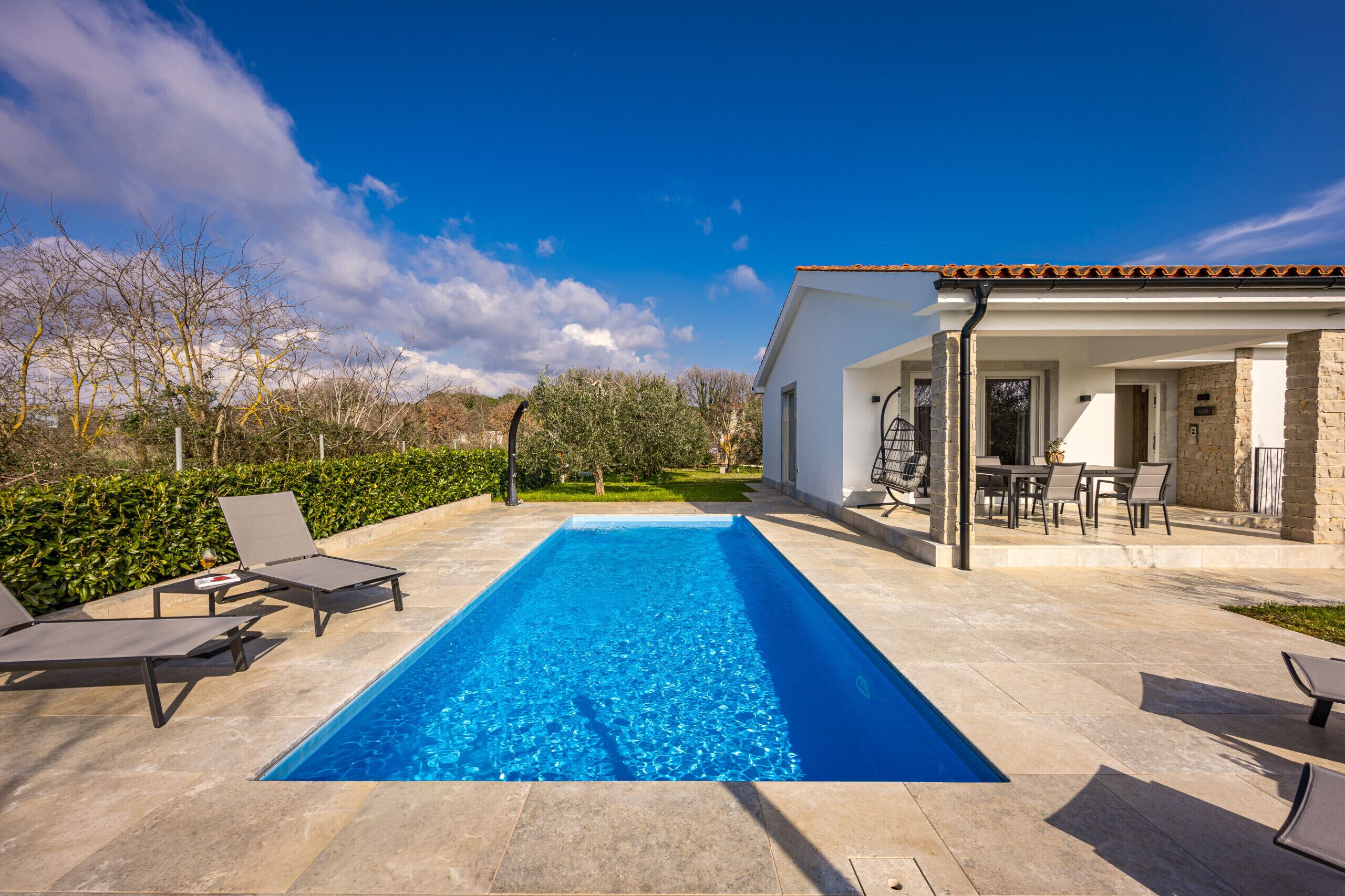 A rectangular swimming pool with lounge chairs and a patio area with a table and chairs.