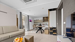 A modern living room with a sofa, a coffee table with fruit, and a dining area with a table and chairs. - Lavanda Harmony Apartment (Pomer)