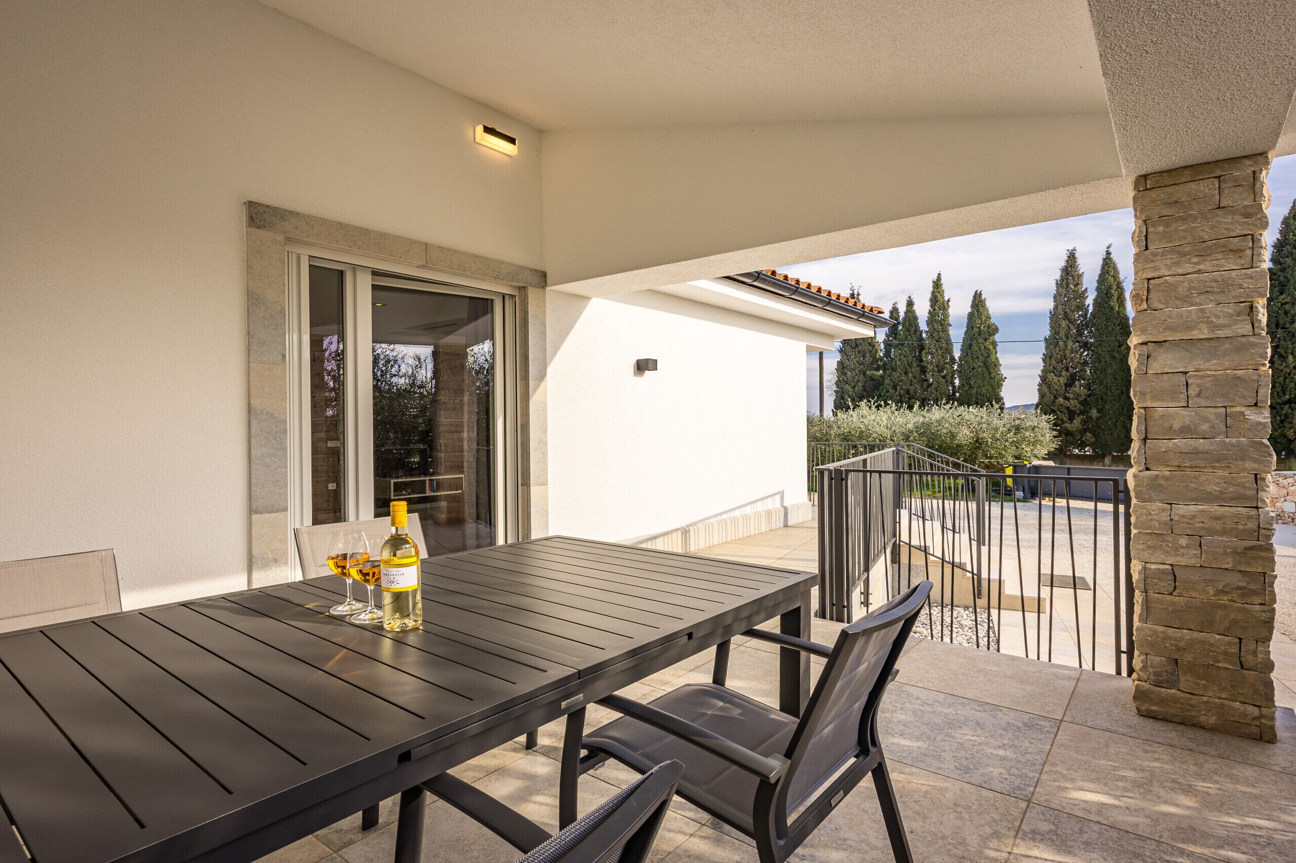 A patio with a table and chairs, a bottle of wine, and a glass.
