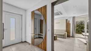 A modern interior with a wooden-framed mirror, a white door, a beige sofa, and a view of the outdoors. - Lavanda Harmony Apartment (Pomer)