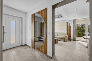 Ein modernes Interieur mit einem spiegelnden, hölzern gerahmten Spiegel, einer weißen Tür, einem beigefarbenen Sofa und Blick ins Freie.
