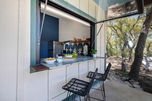 Uma cozinha com janela para um jardim, duas cadeiras pretas e um balcão com comida e bebidas.