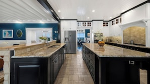 A modern kitchen with granite countertops, dark cabinetry, and a central island. - 5BR Hill Country | Casita, Pool + 3-Building Compound | Sleeps 18 (Dripping Springs)