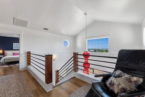 Una habitación con una escalera, una cama, un ventanal con vistas y un adorno rojo.
