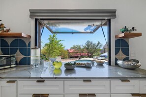 Une cuisine donnant sur un jardin, une fenêtre avec vue et un plan de travail sur lequel se trouvent divers objets.
