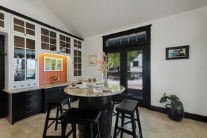 A kitchen with a round island, bar stools, a window with a view, and a door with a black frame.