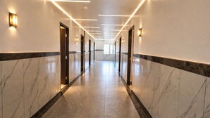 A long, well-lit hallway with marble walls and floors, featuring doors and light fixtures along the sides. - Shahenshah Hotel  (Prayagraj)