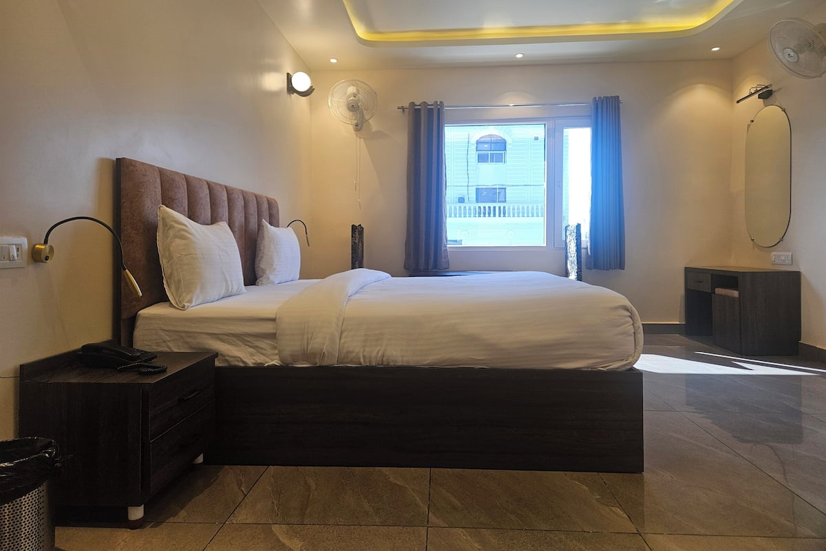 Un dormitorio moderno con una cama grande, lámparas de noche, una mesita de noche, un espejo y un ventanal con cortinas.