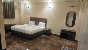 A modern bedroom with a large bed, bedside tables, a mirror, and a ceiling fan. - Shahenshah Hotel  (Prayagraj)