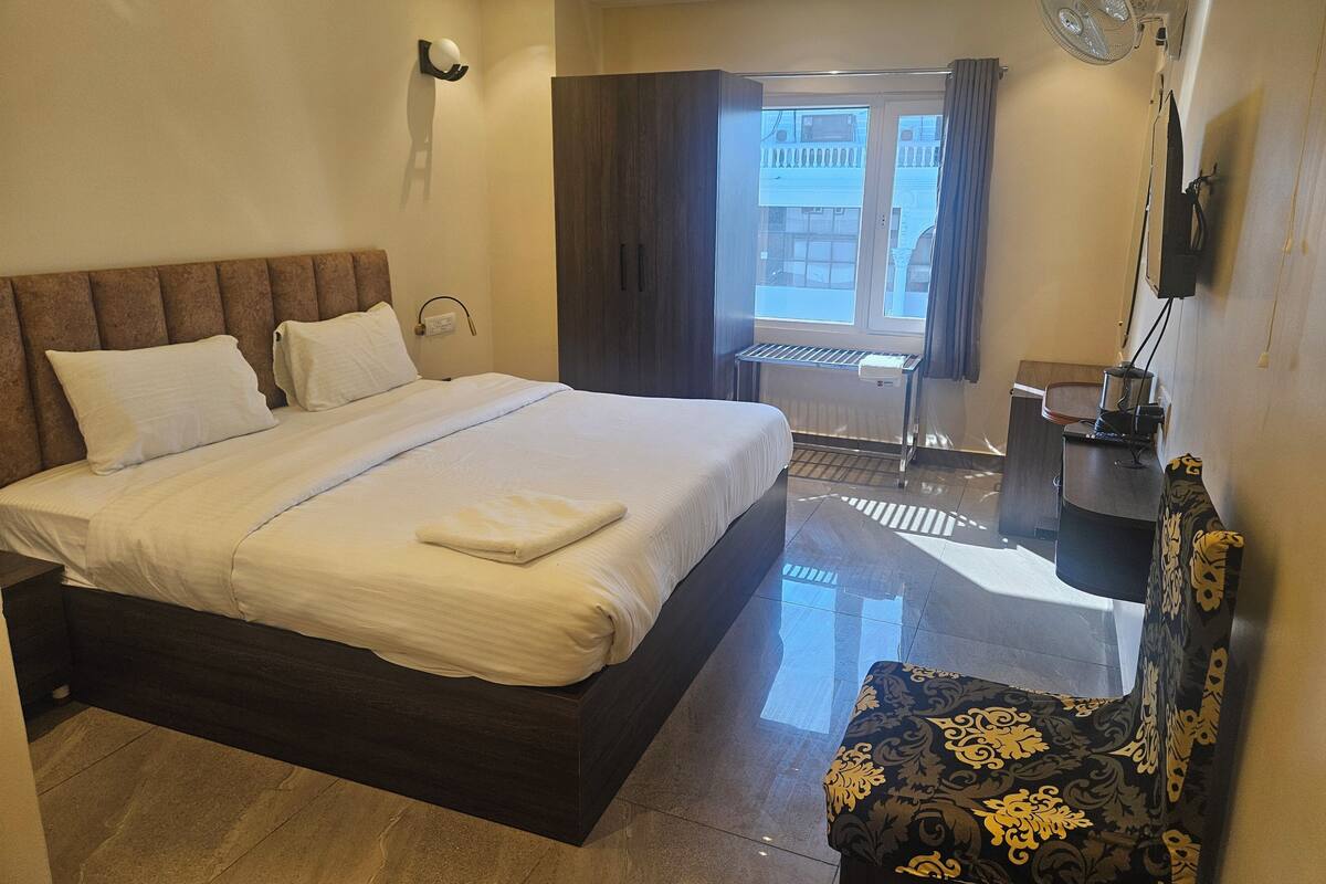 Habitación de hotel con una cama grande, una mesita de noche, una silla, un escritorio y vistas al exterior.