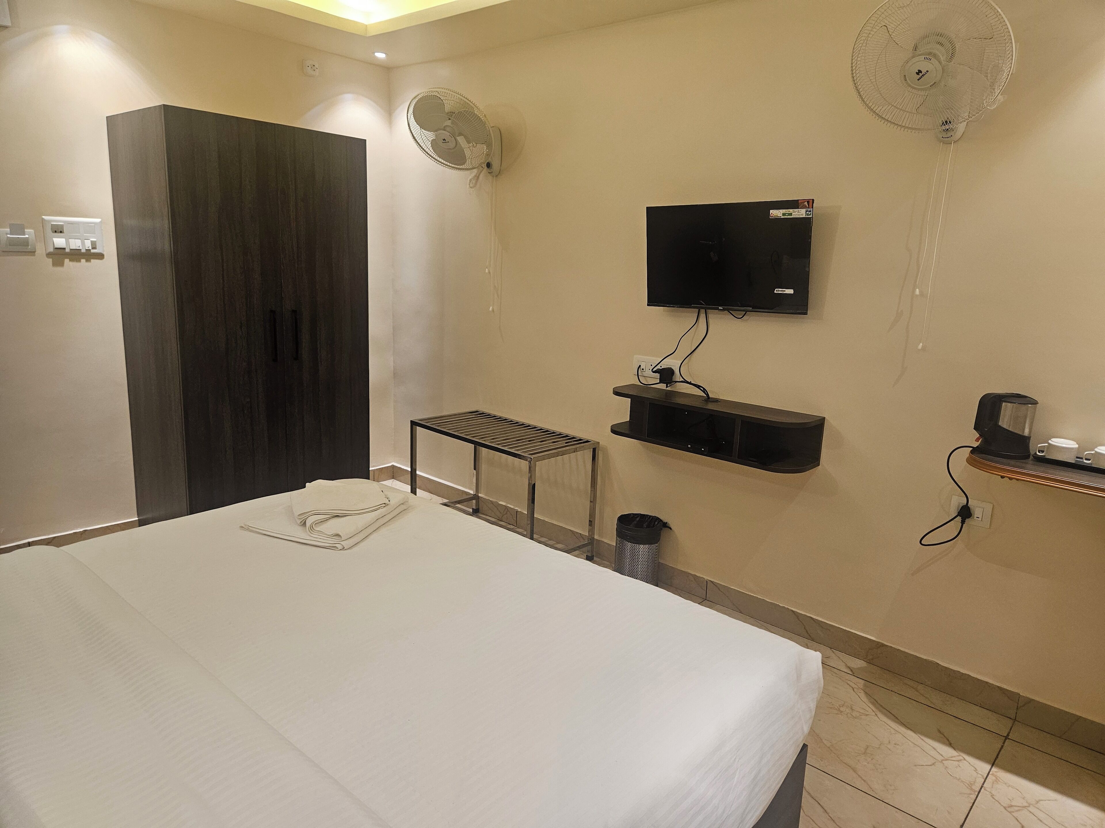 A hotel room with a bed, a TV mounted on the wall, a small table, and a shelf with a coffee maker.