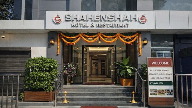 The entrance to Shahenshah Hotel & Restaurant with a welcome sign listing amenities like AC/Non AC rooms, breakfast, lunch, dinner, 100% vegetarian options, and a travel desk. - Shahenshah Hotel  (Prayagraj)