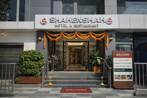 The entrance to Shahenshah Hotel & Restaurant with a welcome sign listing amenities like AC/Non AC rooms, breakfast, lunch, dinner, 100% vegetarian options, and a travel desk. - Shahenshah Hotel  (Prayagraj)
