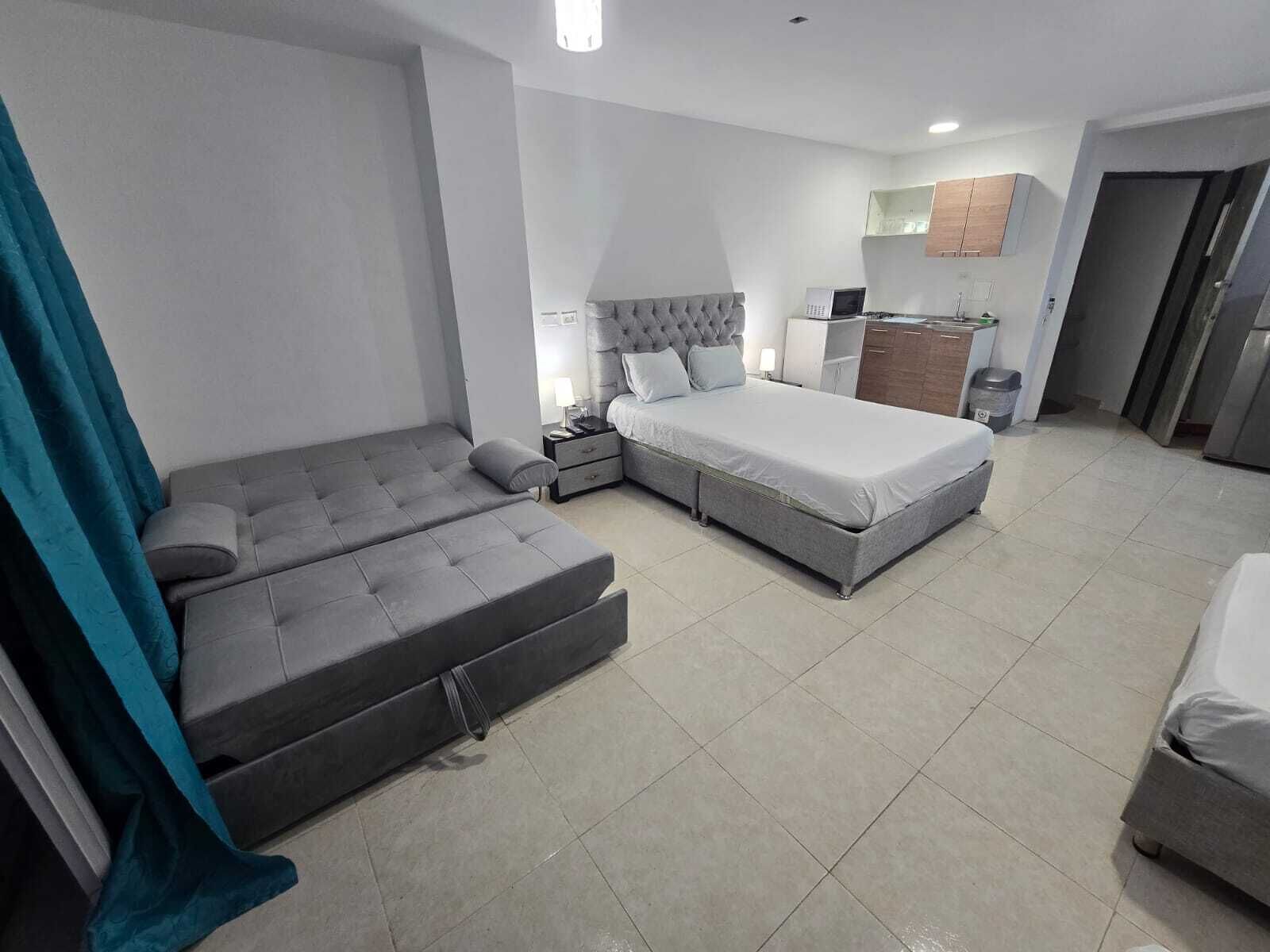 A modern bedroom with a sofa bed, a separate bed, a nightstand, and a small kitchenette.