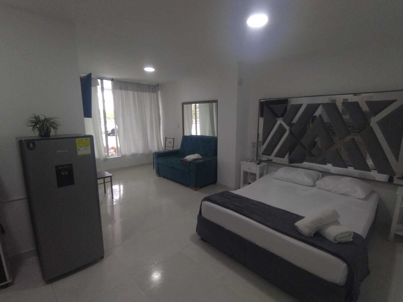 Une chambre d’hôtel équipée d’un lit, d’un bureau, d’une chaise, d’un réfrigérateur et d’une fenêtre avec des rideaux.