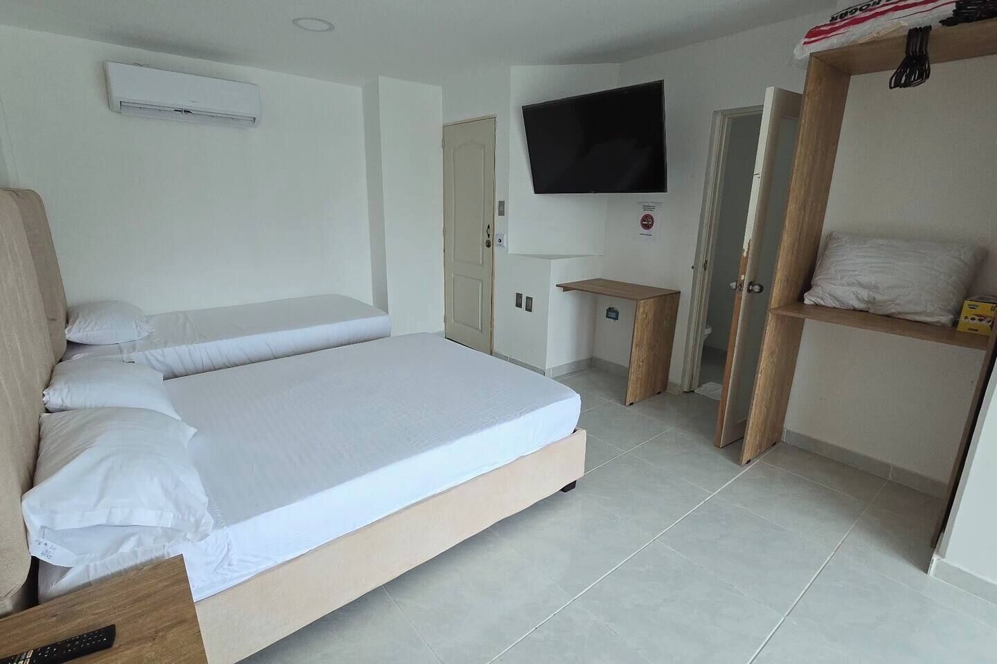 A bedroom with a bed, a TV mounted on the wall, a wooden desk, and a wardrobe.