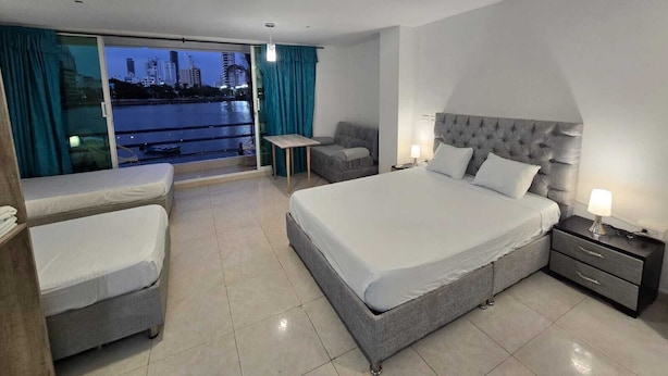Een moderne hotelkamer met een groot bed, een bank, een kleine tafel en uitzicht op een stadsgezicht door een schuifdeur.